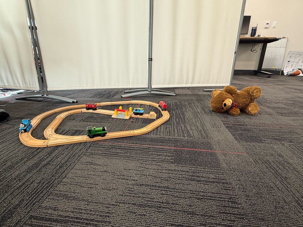 Indoor room with a wooden toy train set and a teddy bear on carpet